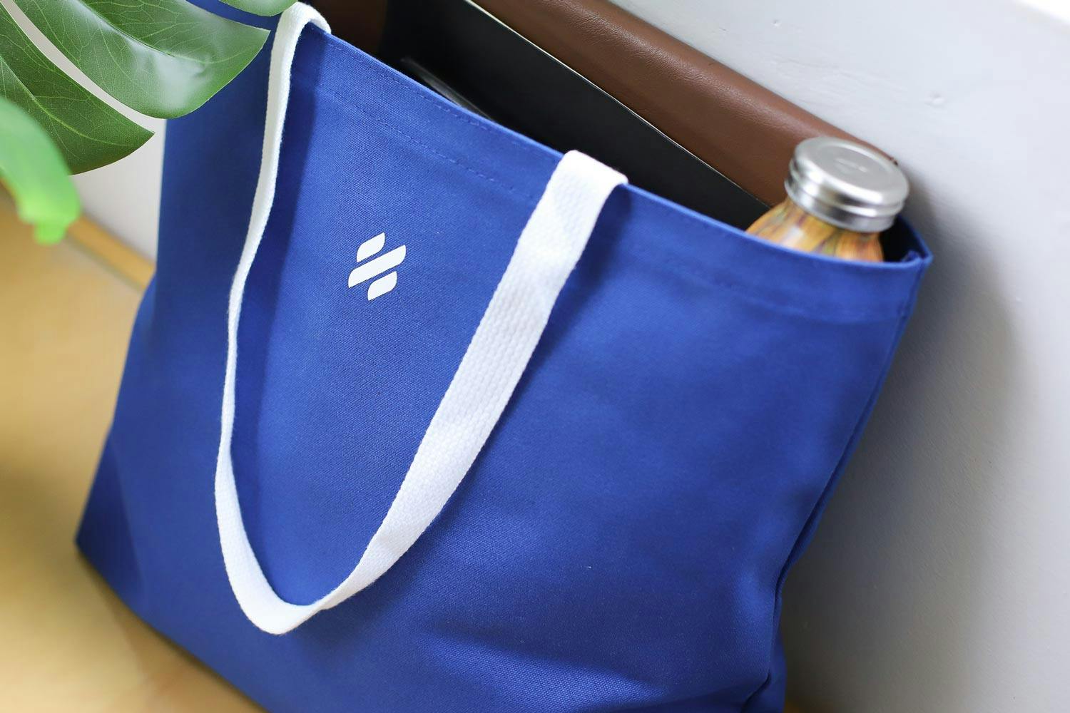 A Help Scout branded tote bag filled with work items like computer and water bottle. A Help Scout branded tote bag filled with work items like computer and water bottle.